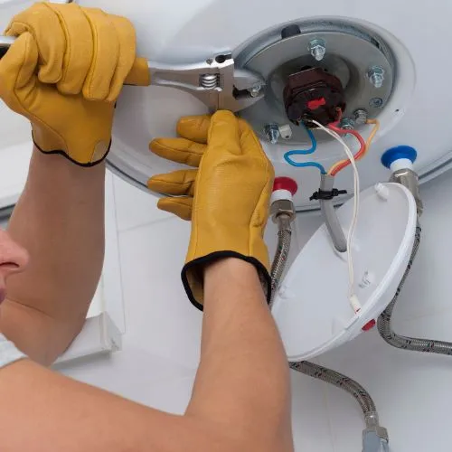 Mains gantées resserrant les fixations d'un ballon d'eau chaude avec une clé