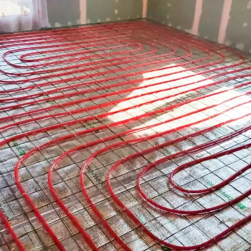 Circuit de tuyaux rouges d'un plancher chauffant posé sur le sol d'une pièce en travaux