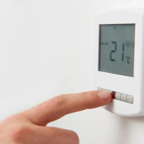 Main réglant un thermostat de chauffage programmable qui affiche 21 °C