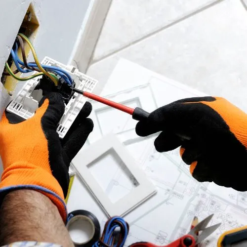 Électricien portant des gants et raccordant les fils d'une prise avec un tournevis